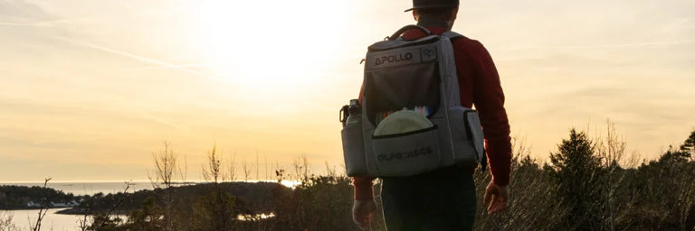En ung mand går med en Alfa Discs taske i solnedgangen ved et strandige