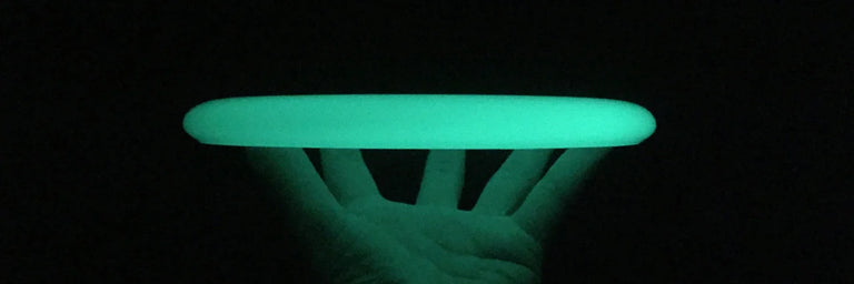 En lysende disc golf disc der bliver holdt i en åben hånd i et mørkt rum