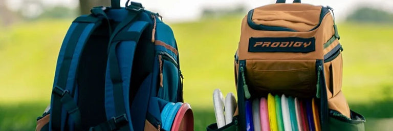 To disc golf tasker fra Prodigy i forskellige farver med en slørret baggrund af et bakket landskab